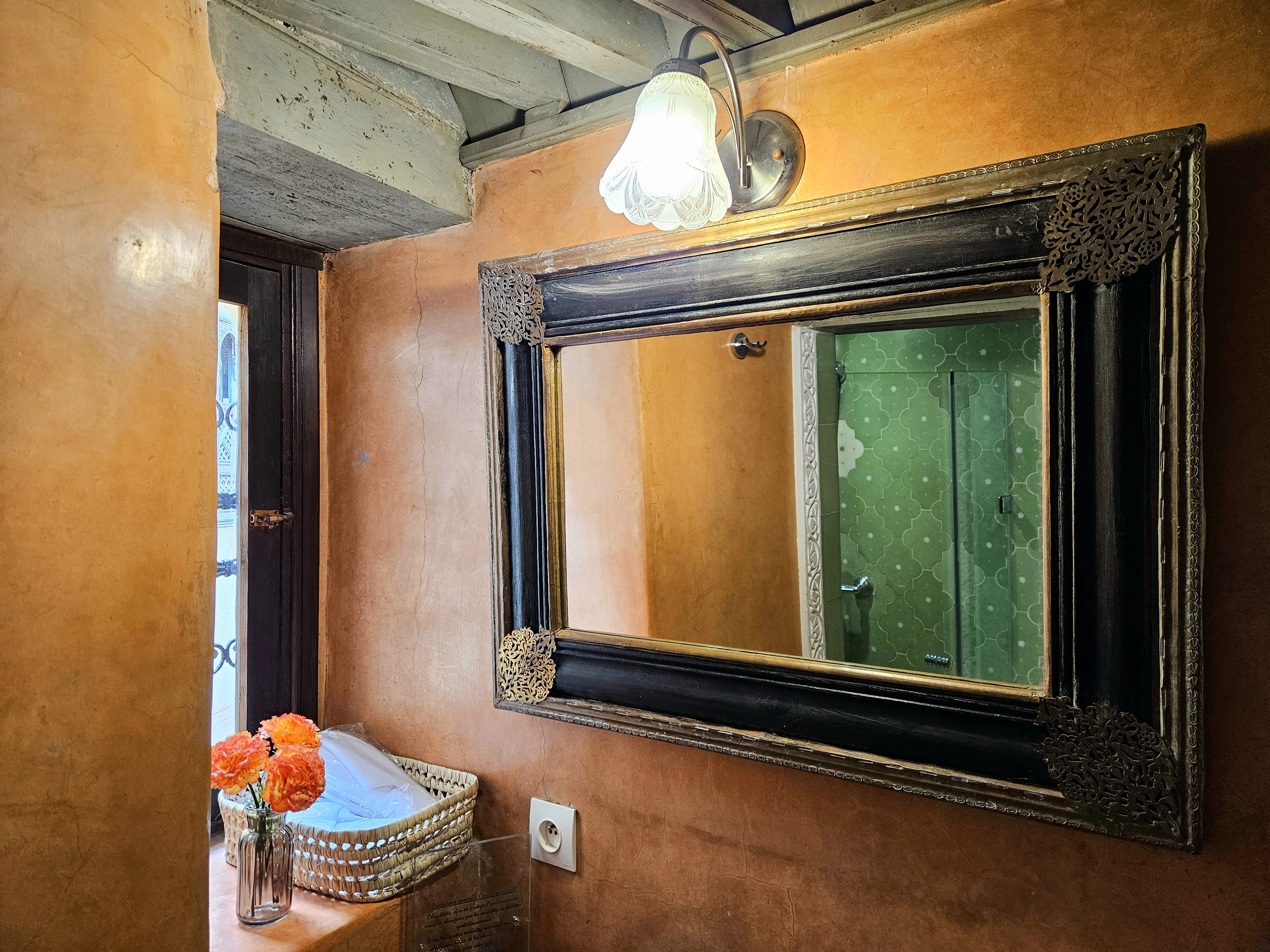 Carved wood and brass mirror with fresh flowers and courtesy amenity basket in Chambre Jade bathroom