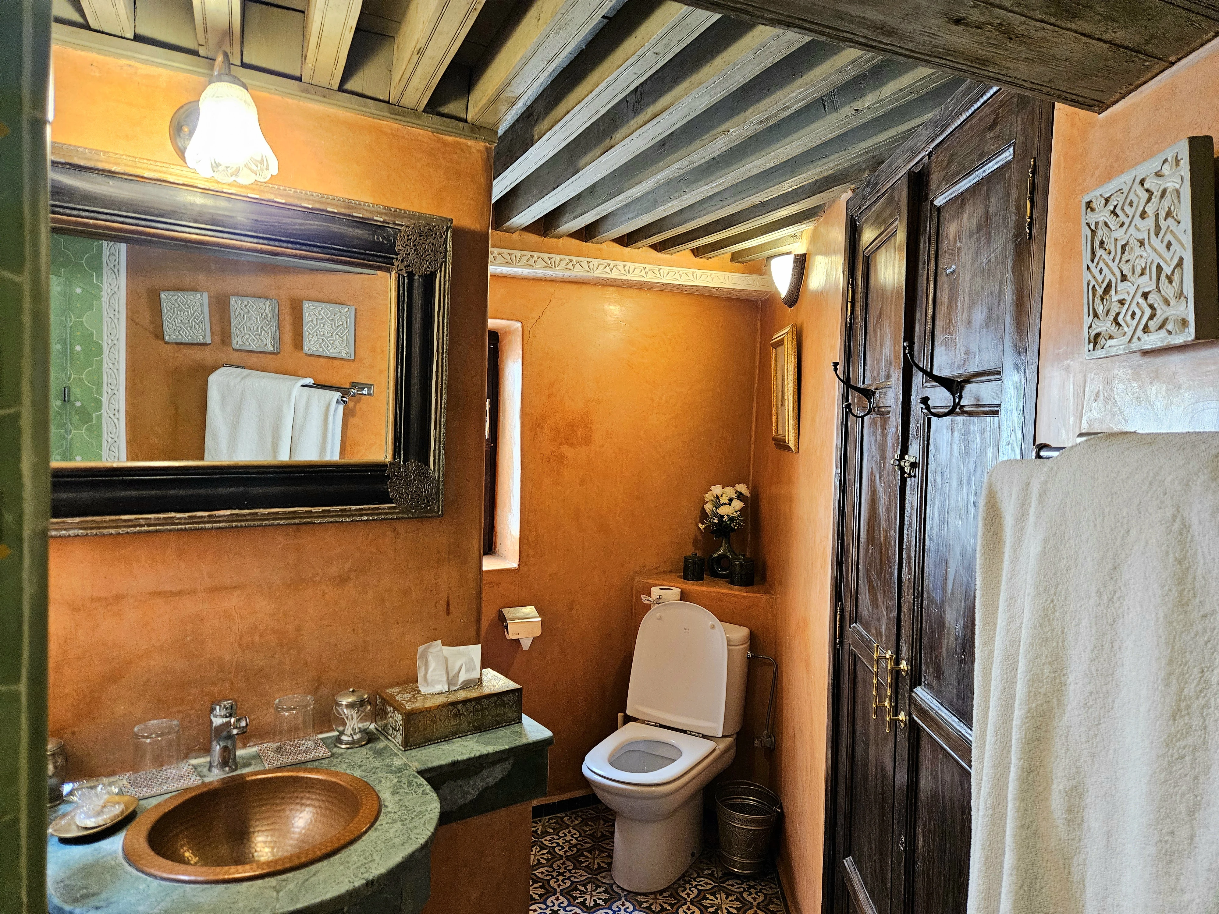 Moroccan bathroom vanity with hand-hammered copper sink, carved mirror, and cedar woodwork in Chambre Jade