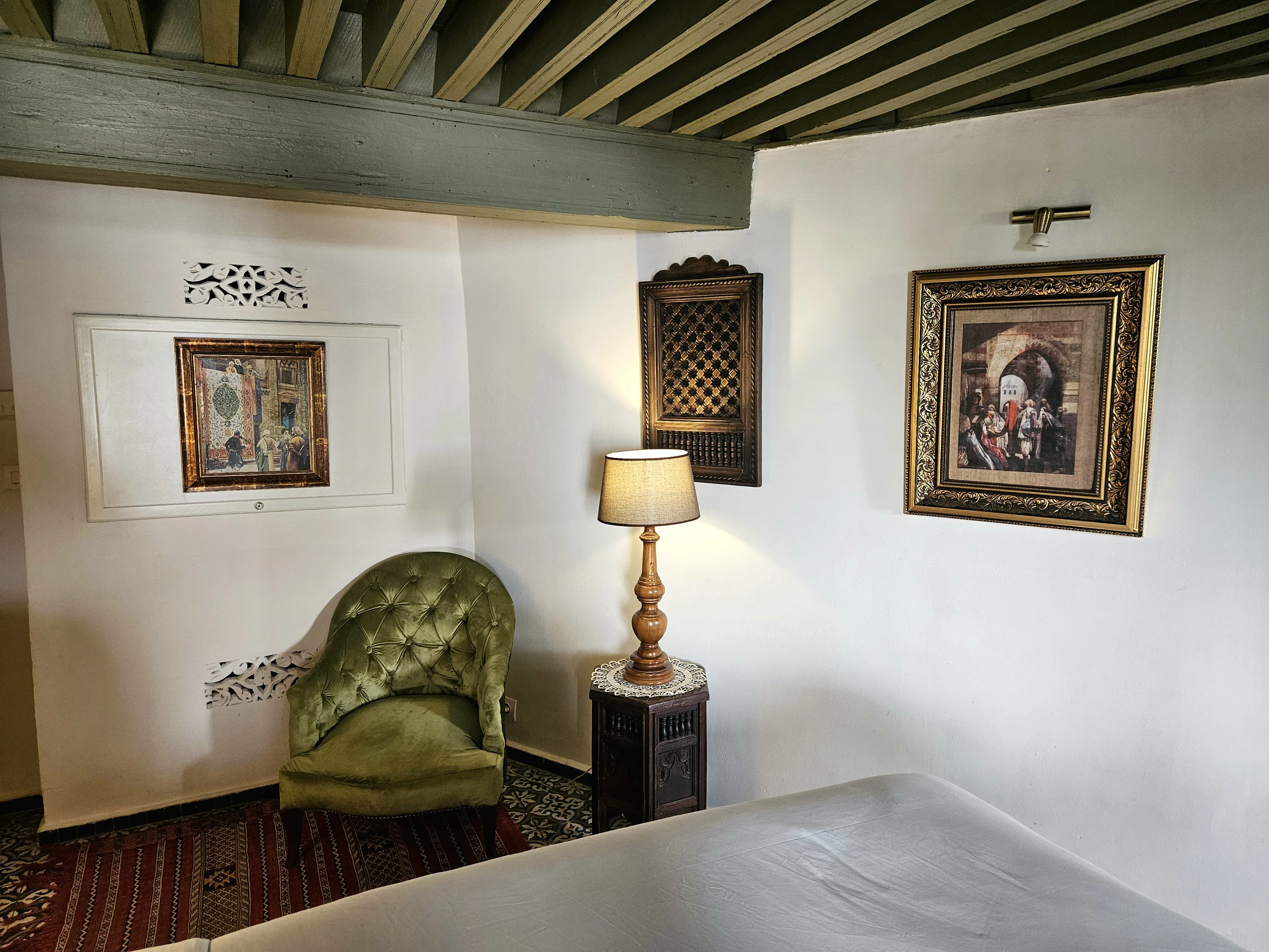 Cozy green velvet armchair and hand-carved Moroccan nightstand in Chambre Jade at Riad Le Calife in Fes