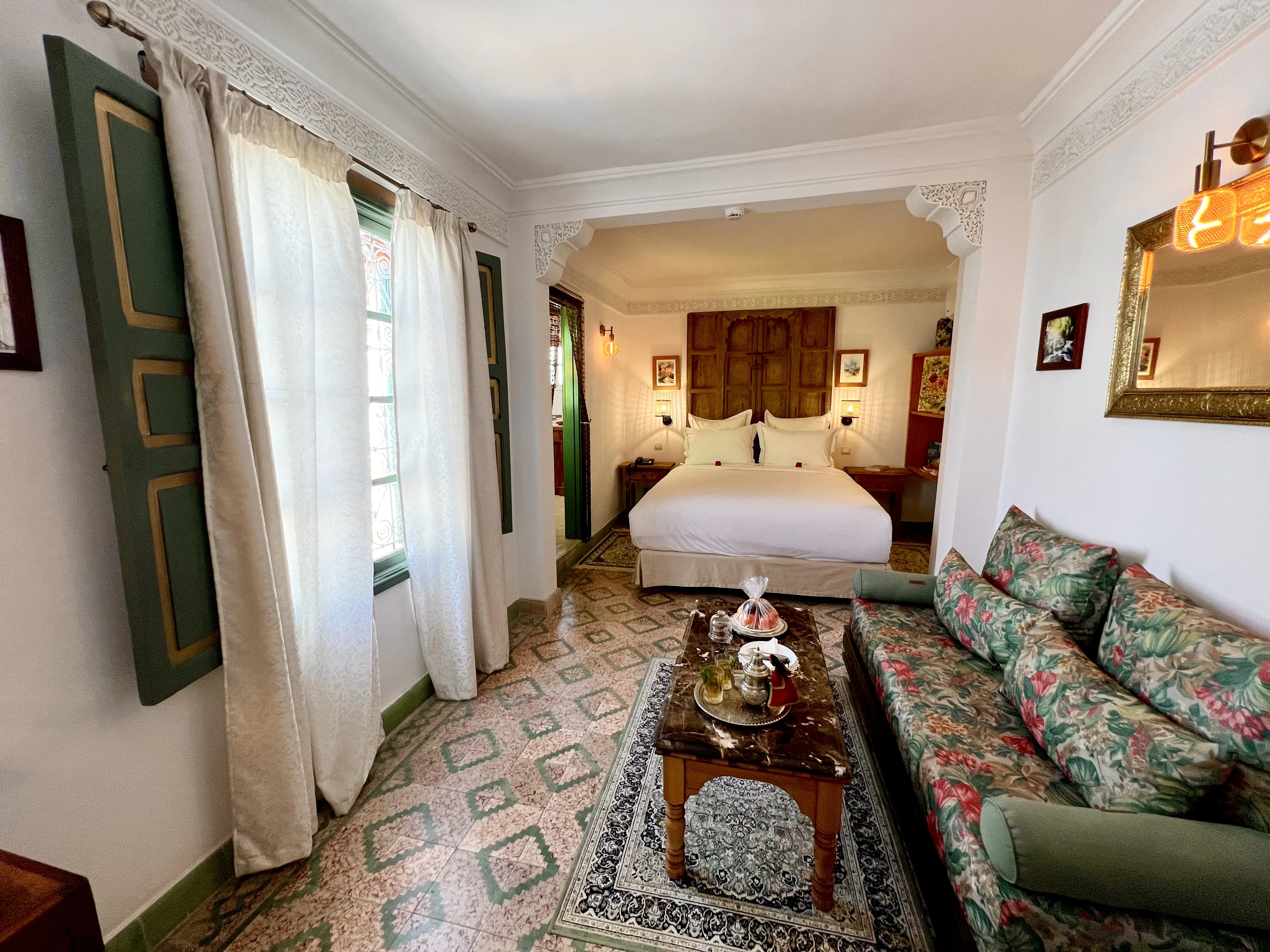 Spacious 28 sqm Chambre Menzeh at Riad Le Calife showing floral sofa, marble tea table, terrace shutters, and double bed in alcove