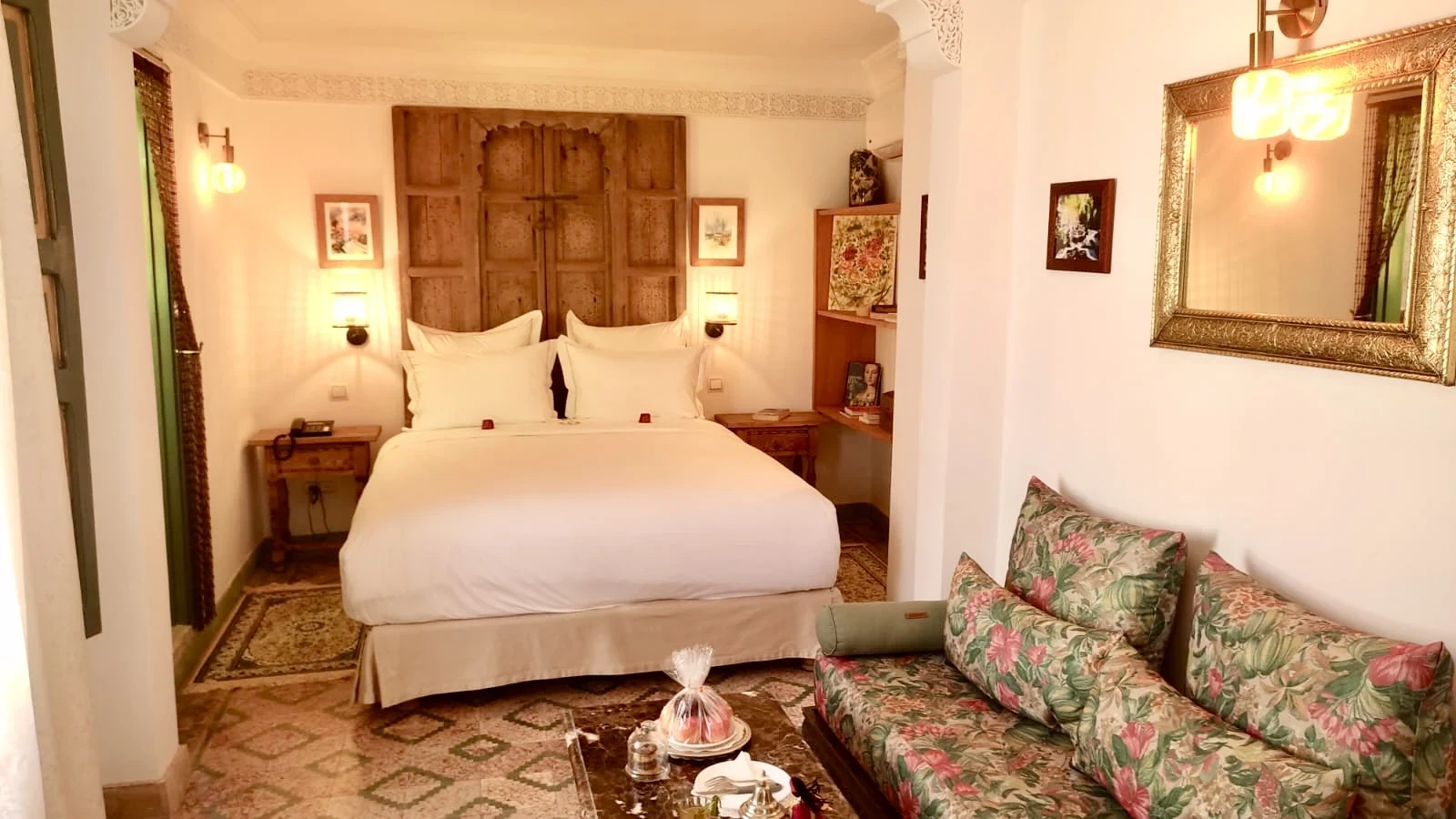 Comfortable floral upholstered sofa, marble coffee table, and gilded artisan mirror in Chambre Menzeh at Riad Le Calife