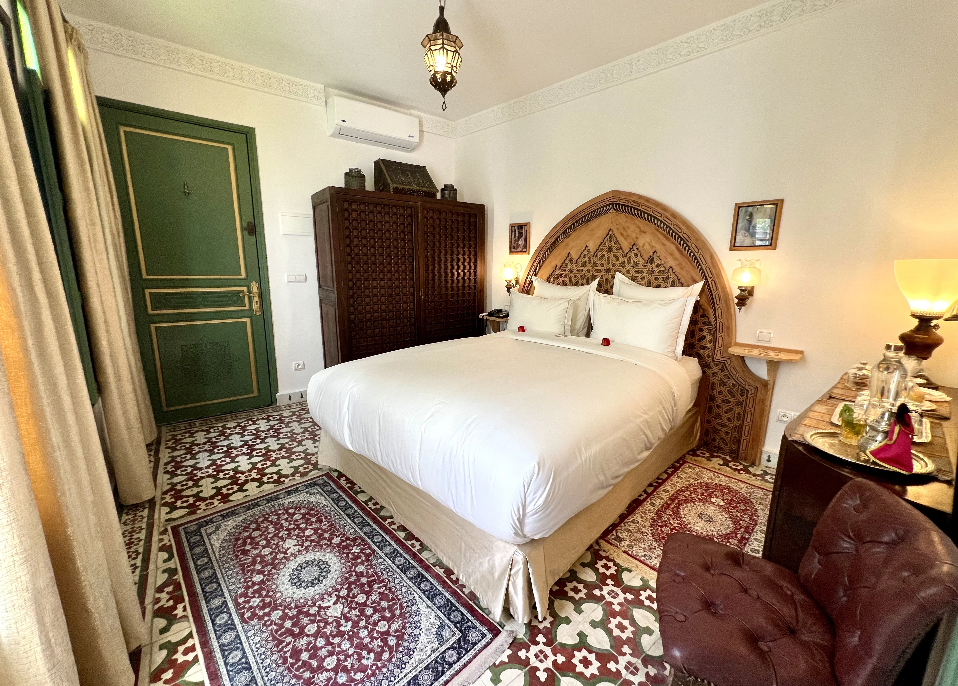Wide bedroom angle of Chambre Saphir showing wooden moucharabieh dressing wardrobe, double bed, tufted armchair, and welcome tea tray