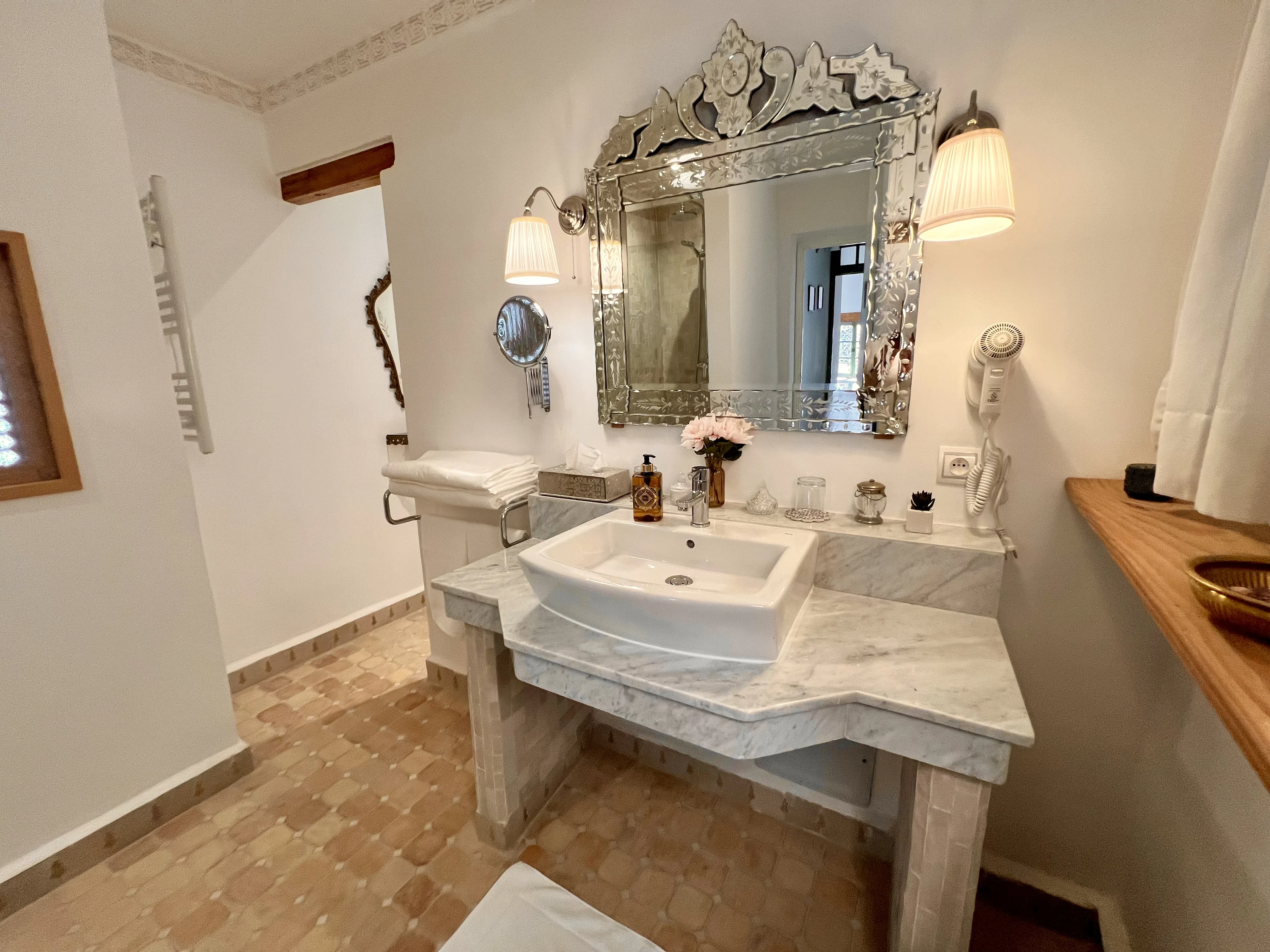 Private en-suite bathroom in Suite Ivoire with white marble vanity counter, Venetian etched mirror, modern sink, and luxury amenities