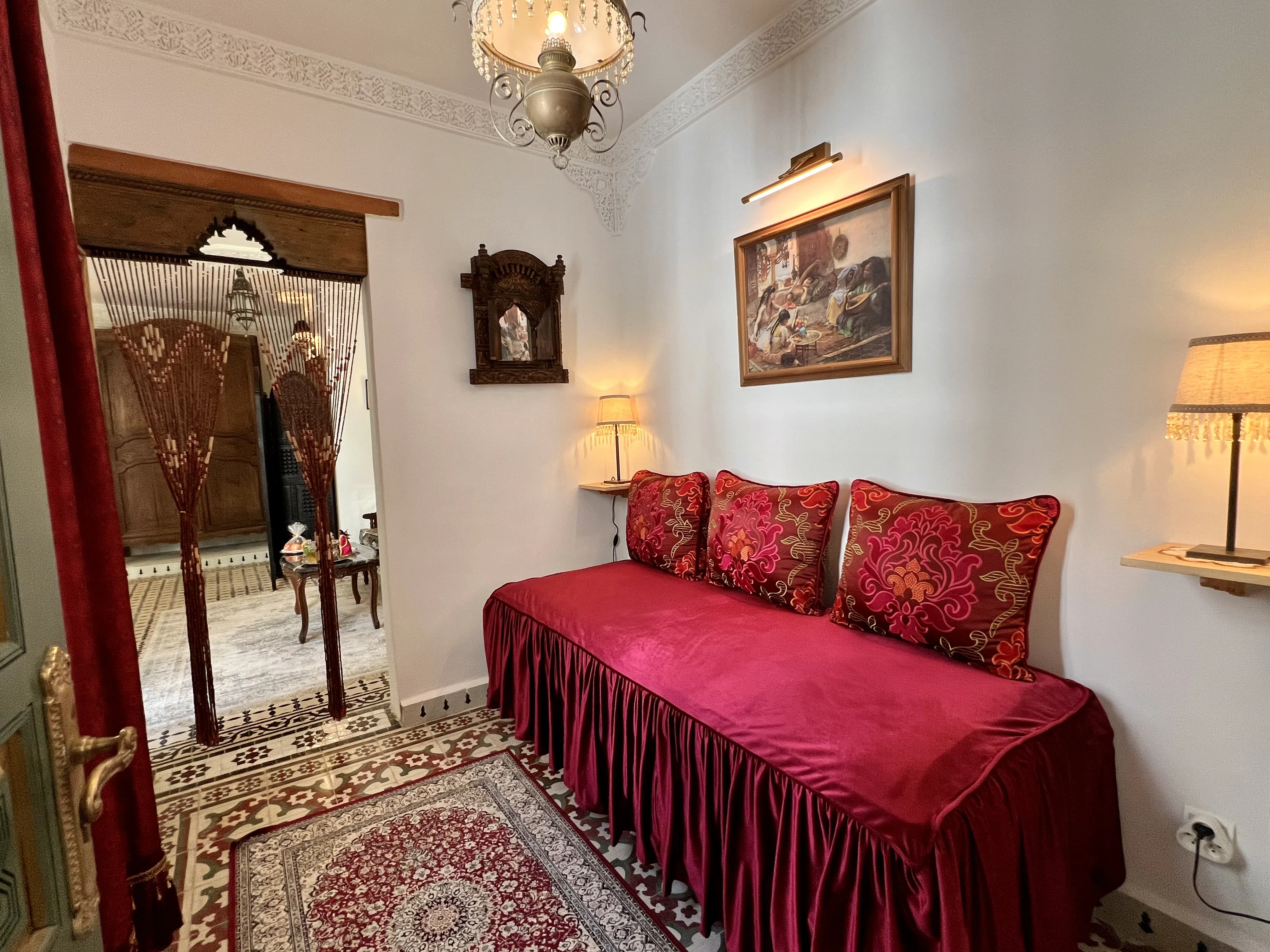 Intimate boudoir lounge in Suite Ivoire with velvet crimson daybed, embroidered pillows, oriental carpet, and carved archway