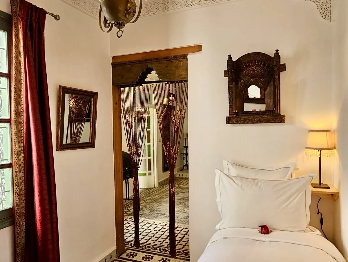 Charming bedroom alcove and carved wooden archway in Suite Ivoire with beaded curtain opening towards the grand salon and patio