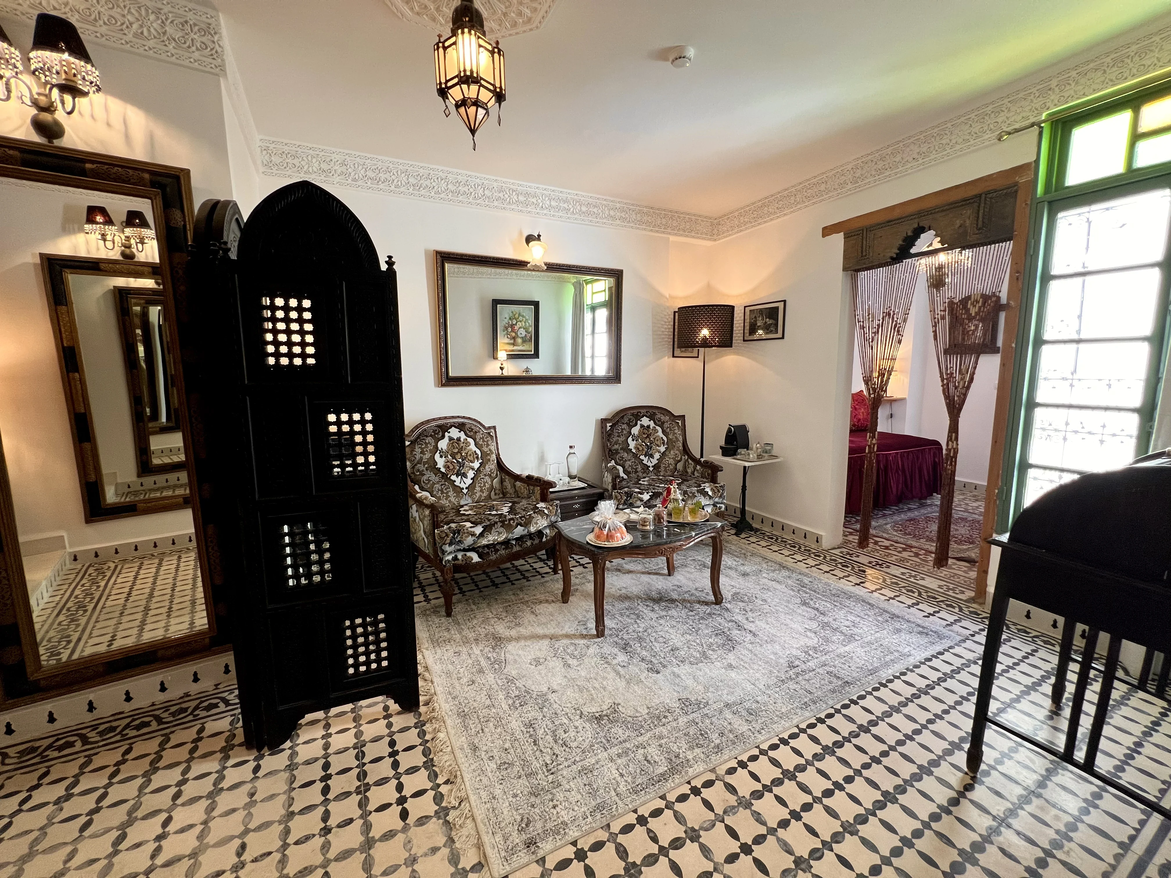 Elegant grand salon in Suite Ivoire featuring antique armchairs, carved moucharabieh screen, writing desk, and Moroccan tea service